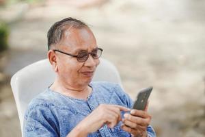 un homme âgé utilise joyeusement un smartphone sur une chaise de jardin. notion de réseau social.
