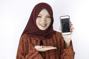 jeune femme islamique asiatique sourit en pointant sur un smartphone debout sur fond blanc. photo