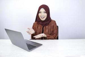 jeune femme islamique asiatique sourit en pointant la main lorsqu'elle travaille sur un ordinateur portable sur fond blanc. photo