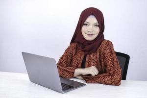 jeune femme islamique asiatique est assise et sourit en travaillant sur un ordinateur portable sur fond blanc. photo