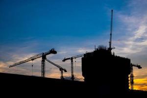 grues de construction industrielle et silhouettes de bâtiments au coucher du soleil photo