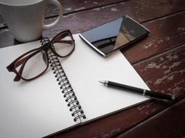espace de travail avec lunettes, stylo, smartphone et tasse à café, papier à lettres et cahier sur une vieille table en bois photo