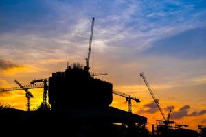 grues de construction industrielle et silhouettes de bâtiments au coucher du soleil photo