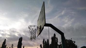 vue latérale d'un vieux panier de basket-ball vert foncé et d'un filet cassé avec un fond sombre du ciel du matin dans le terrain de sport public. photo