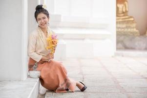 femme thaïlandaise en robe thaïlandaise se reposant dans un temple après avoir utilisé de la poudre soluble dans l'eau sur les joues pour s'amuser à célébrer le festival de l'eau de songkran photo