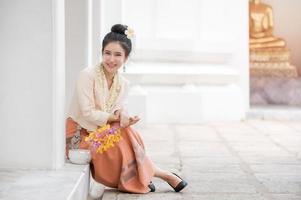 femme thaïlandaise en robe thaïlandaise se reposant dans un temple après avoir utilisé de la poudre soluble dans l'eau sur les joues pour s'amuser à célébrer le festival de l'eau de songkran photo