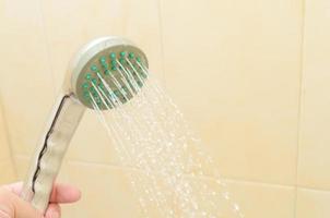 gros plan sur un homme tenant un pommeau de douche dans la cabine de la salle de bain.un jet d'eau se déverse de la douche. photo