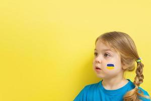 fille de 3 ans avec un drapeau peint en jaune et bleu de l'ukraine sur ses joues sur un fond jaune avec un espace de copie photo