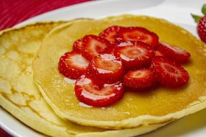 détail de fraises et de crêpes au sirop sur la plaque blanche photo