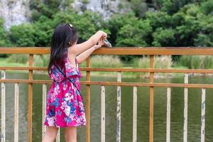 dos d'une adorable petite fille asiatique s'amusant à nourrir et à donner de la nourriture aux poissons dans l'étang photo