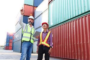 deux travailleurs portant un gilet de sécurité et un casque discutant dans la cour de conteneurs de fret d'expédition logistique. ingénieur travailleur asiatique âgé et sérieux parlant avec son patron sur le lieu de travail. photo