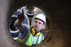 ingénieur industriel hommes portant un casque de sécurité tout en se tenant dans une usine industrielle lourde. la maintenance du travail sur des machines industrielles et la configuration du système de sécurité en usine. photo