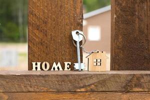 porte-clés de maison en bois sur clôture avec clé et inscription en lettres anglaises maison. chalet en arrière-plan. construction, projet, déménagement dans une nouvelle maison, hypothèque, location et achat immobilier.