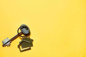 porte-clés en forme de maison en bois avec clé sur fond jaune. construction, conception, projet, déménagement dans une nouvelle maison, hypothèque, location et achat immobilier. copie espace