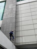 photo d'un ouvrier nettoyant l'extérieur du bâtiment, suspendu à une corde de sécurité