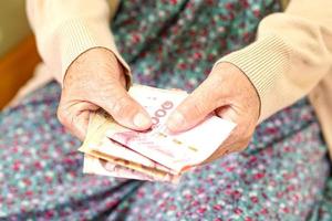 aînée asiatique femme âgée patiente tenant des billets de banque dans sa main, coût de la vie et soins médicaux. photo