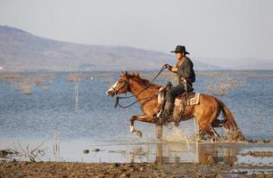 cow-boy à cheval contre un beau coucher de soleil, cow-boy et cheval à la première lumière, montagne, rivière et style de vie avec fond de lumière naturelle photo