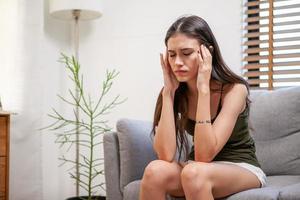 triste jeune femme déprimée à la maison assise sur un canapé. fille frustrée et malheureuse avec de terribles migraines ou maux de tête.