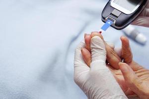 le médecin porte des gants à l'aide d'une lancette au doigt pour vérifier le taux de sucre dans le sang par un lecteur de glycémie. photo