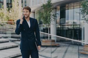 homme d'affaires mal rasé à la mode utilise les technologies modernes a une conversation téléphonique tient un gadget photo