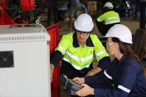 trois ingénieurs et ouvriers multiculturels de l'industrie lourde dans un bras de robot automatique à contrôle uniforme pour l'utilisation en usine. l'entrepreneur industriel féminin utilise une tablette.