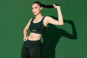 belle forte joyeuse joyeuse jeune femme sportive asiatique fait des exercices isolés sur fond vert. fille de fitness en tenue de sport posant à l'intérieur. mouvement, force et motivation. photo