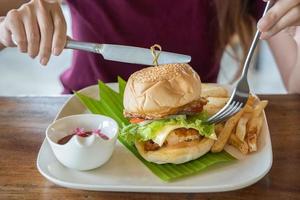 couteau et fourchette couverts dans les mains avec burger sur congé de banane avec bol de sauce tomate en assiette blanche photo