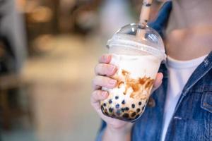 jeune femme tient, boit du thé au lait à bulles de perle de tapioca aromatisé à la cassonade avec de la paille de verre sur le marché nocturne de taiwan, gros plan, bokeh photo