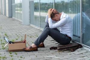 l'employé de bureau licencié est tombé à genoux et s'est couvert le visage à cause du stress. devant lui se trouve une boîte en carton avec du papier à lettres. l'homme est mécontent en raison d'une réduction du robot. photo