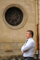 séance photo de mariage sur le fond de l'ancien bâtiment. le marié regarde sa mariée poser. photographie de mariage rustique ou bohème.