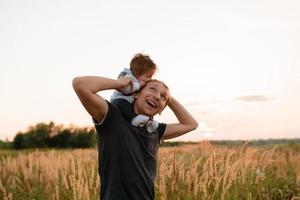 une petite fille mignonne est assise sur son cou près de son père. père et fille marchent dans le champ photo