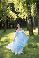 femme enceinte au chapeau posant dans une robe sur fond d'arbres verts. photo