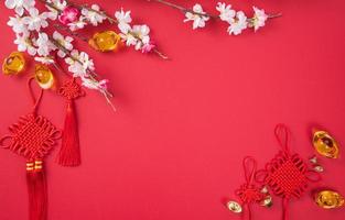 concept de design du nouvel an lunaire chinois - beau noeud chinois avec fleur de prunier isolé sur fond rouge, mise à plat, vue de dessus, mise en page aérienne. photo