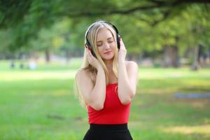 belle femme blonde debout tout en écoutant de la musique sur le casque au parc. photo