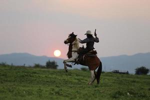 cow-boy à cheval avec une main tenant un pistolet sur fond de coucher de soleil. photo