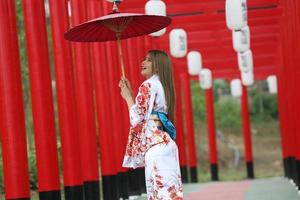 jeune fille asiatique portant des vêtements traditionnels japonais kimono et un parapluie rouge. photo