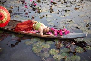 jeunes femmes asiatiques en costume traditionnel dans le bateau et fleurs de lotus roses dans l'étang. belles filles en costume traditionnel. fille thaïlandaise en robe thaïlandaise rétro, fille thaïlandaise en costume traditionnel photo