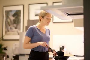 vue latérale portrait de femmes dans son dîner de cuisine debout près d'une cuisinière et cuisinant sur une plaque de cuisson à gaz mur carrelé blanc avec lumière chaude photo