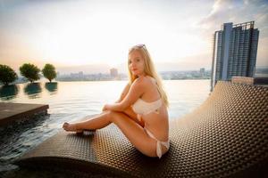 jeune femme appréciant et relaxant au bord de la piscine. modèle de jeune fille mince en bikini blanc au bord de la piscine. photo