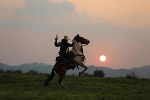 cow-boy à cheval contre un beau coucher de soleil, cow-boy et cheval à la première lumière, montagne, rivière et style de vie avec fond de lumière naturelle photo
