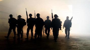 silhouettes de soldats de l'armée dans le brouillard contre un coucher de soleil, équipe de marines en action, feu et fumée entourés, tir avec fusil d'assaut et mitrailleuse, attaque ennemie photo