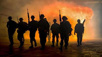 silhouettes de soldats de l'armée dans le brouillard contre un coucher de soleil, équipe de marines en action, feu et fumée entourés, tir avec fusil d'assaut et mitrailleuse, attaque ennemie photo