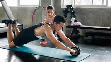 couple d'athlètes sportifs faisant de l'exercice avec une roue à rouleaux abs pour renforcer leurs muscles abdominaux dans la salle de sport. photo