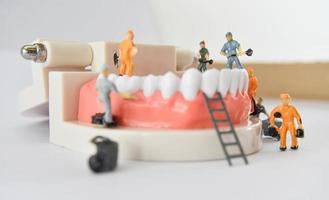 personnes miniatures pour réparer une dent ou un petit travailleur de la figure nettoyant le modèle de dent comme médical et de soins de santé. photo