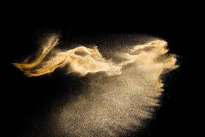 nuage de sable abstrait.éclaboussures de sable de couleur dorée sur fond sombre.vague de mouche de sable jaune dans l'air. le sable explose sur fond noir, jetant le concept de mouvement d'arrêt de gel. photo