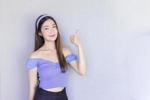 une jeune belle femme asiatique vêtue d'une chemise violette agit comme un bon symbole et une autre main montre qu'elle présente quelque chose en arrière-plan. photo