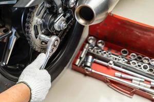 Mécanicien à l'aide d'une clé et d'une douille sur le pignon de moto. Concept d'entretien et de réparation dans le garage de motos. Mise au point sélective photo