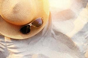 Chapeau d'été chapeau de paille fasion et accessoires de lunettes de soleil sur fond de mer de plage de sable