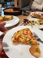 Tranche fraîchement cuite de pizza suprême à croûte mince assise sur une assiette blanche avec une fourchette photo