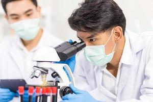 chercheurs en soins de santé travaillant dans des laboratoires de sciences biologiques, un chercheur utilise un microscopique et son assistant utilisant une tablette pour analyser les informations sur le virus en laboratoire photo